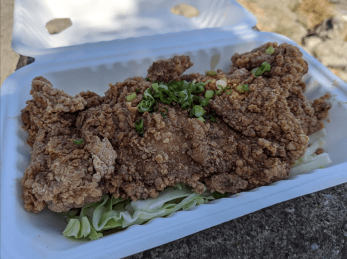 A container holding a piece of crispy fried chicken topped with green onions on a bed of lettuce.