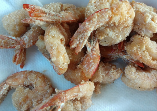 A close-up of crispy, golden-brown fried shrimp on a paper towel.