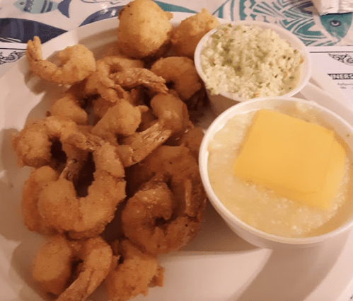 A plate of fried shrimp with coleslaw and a side of grits topped with a slice of cheese.