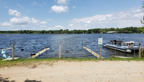 A serene lake view with docks, a boat, and trees under a partly cloudy sky.