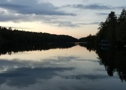 A serene lake at dusk, reflecting trees and clouds under a soft, colorful sky.