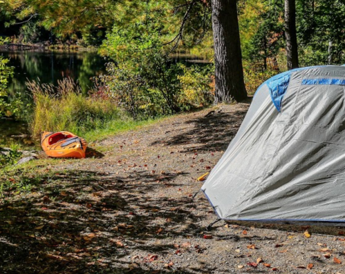 A tent by a serene lake, with an orange kayak resting nearby amidst colorful autumn foliage.