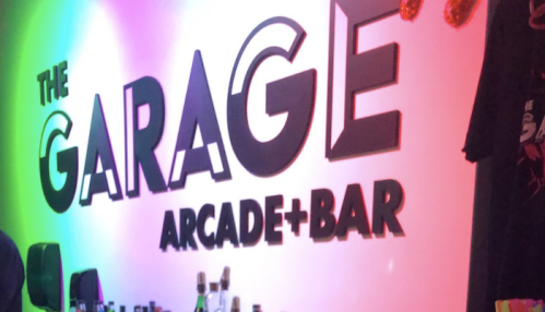 Colorful wall sign for "The Garage Arcade + Bar" with a vibrant atmosphere and bar setup in the foreground.