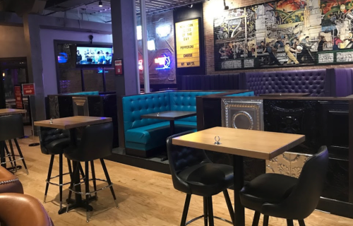 Interior of a bar with blue and purple seating, wooden tables, and a TV on the wall.