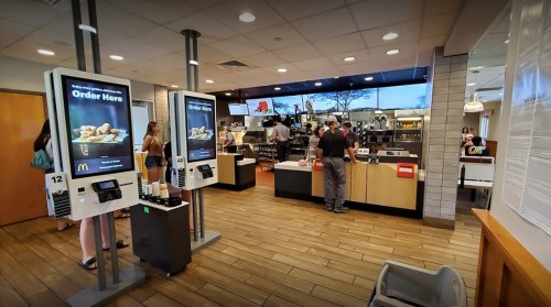 Interior of a McDonald's restaurant with self-order kiosks and customers at the counter. Bright and modern design.