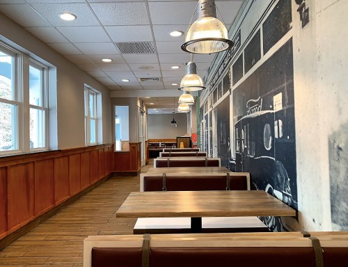 Interior of a restaurant featuring wooden tables, benches, and a large black-and-white mural on the wall.