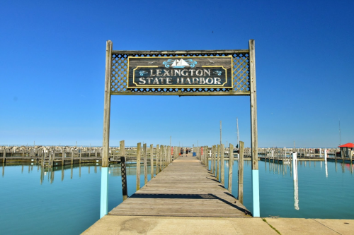 Sign for Lexington State Harbor at the end of a wooden pier, with calm water and clear blue skies in the background.
