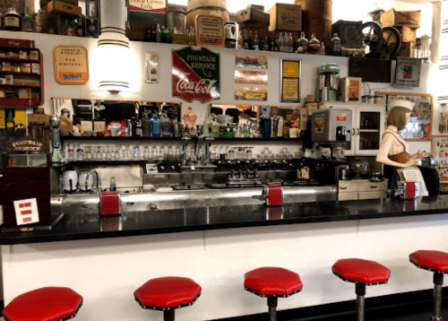 A vintage diner counter with red stools, retro decor, and a soda fountain, evoking a nostalgic atmosphere.