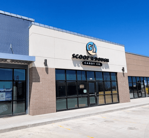 Exterior of Scoop 'n Dough Candy Co. building with large windows and a blue sky in the background.