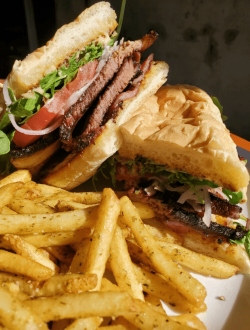 A close-up of a sandwich with brisket, lettuce, and tomato, served with a side of golden fries.