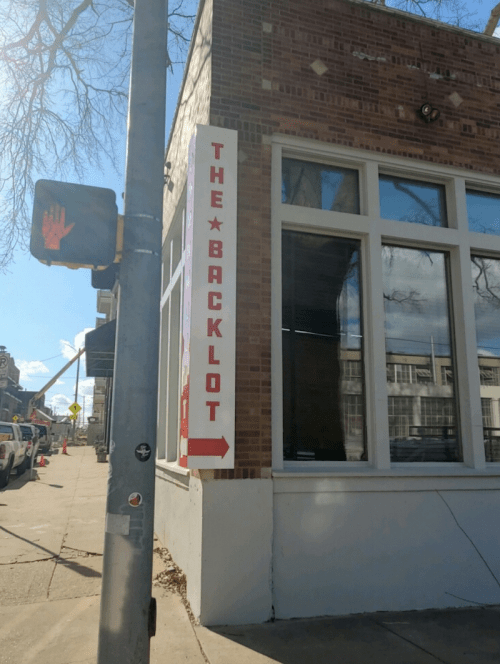 Sign for "The Backlot" on a brick building corner, with a directional arrow pointing left.