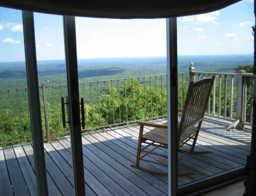 A rocking chair on a wooden deck overlooking a vast green landscape under a clear blue sky.