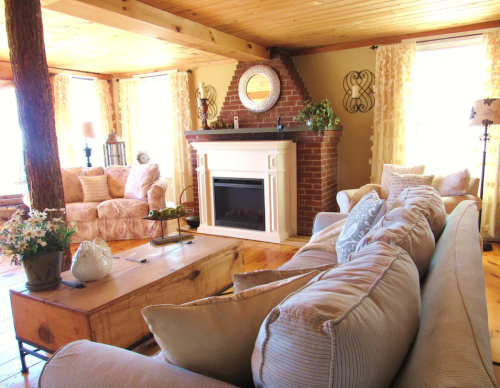 Cozy living room with a brick fireplace, wooden beams, and comfortable seating, featuring warm lighting and decorative accents.