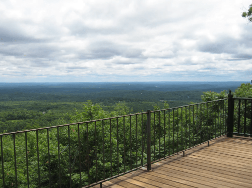 A scenic view from a wooden deck overlooking a lush green landscape under a cloudy sky.