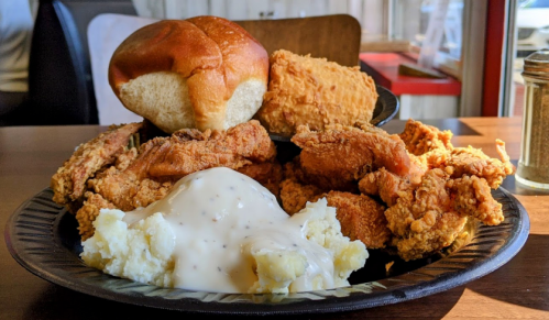 A plate of fried chicken, a biscuit, a piece of fried food, and mashed potatoes with gravy.