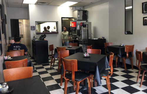 A cozy restaurant interior with black and white checkered floors, wooden tables, and a counter in the background.