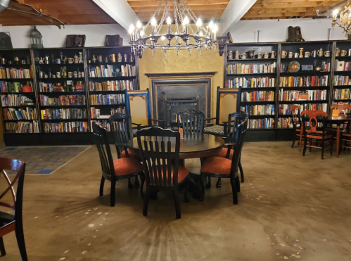 Cozy library with a round table and chairs, surrounded by bookshelves filled with books and a fireplace.