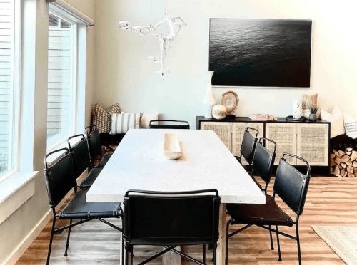 A modern dining room with a large table, black chairs, and minimalist decor, featuring a wall-mounted artwork.