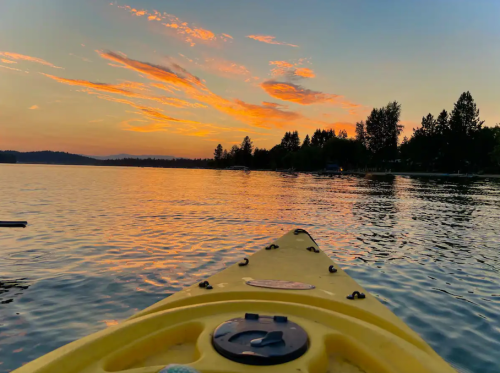 A yellow kayak on calm water at sunset, with vibrant clouds and trees reflected in the lake.