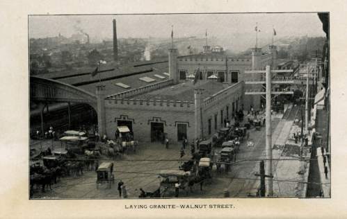 Historic black-and-white image of Walnut Street with horse-drawn carriages and a large building under construction.