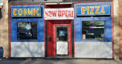 Front view of Cosmic Pizza with a "Now Open!" banner, featuring blue and red exterior and large windows.