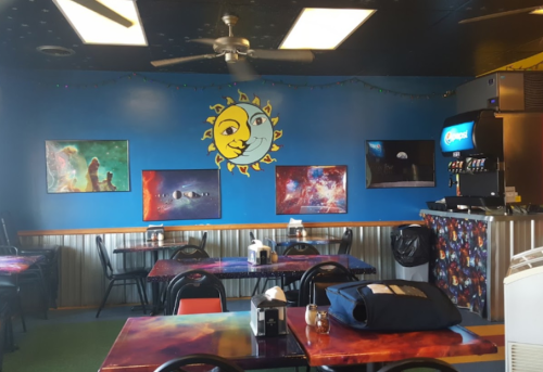 Colorful restaurant interior featuring space-themed artwork, a sun mural, and tables with vibrant designs.