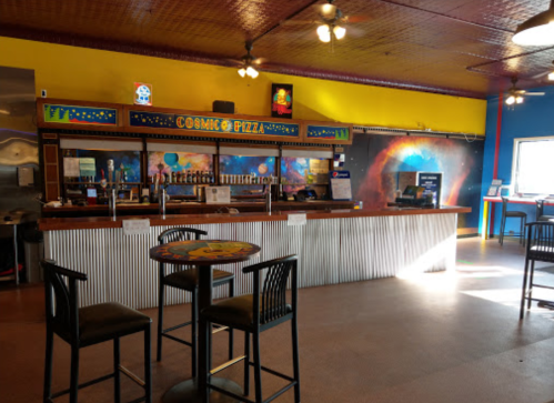 A colorful pizza restaurant interior with a bar, tables, and a cosmic-themed mural on the wall.