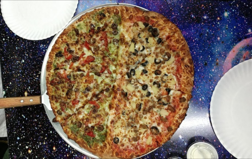 A large pizza with various toppings, including vegetables and meats, on a colorful, space-themed table.