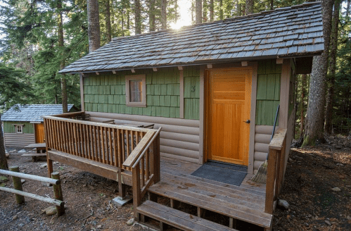 A cozy cabin with a wooden deck, nestled among tall trees in a forest setting.