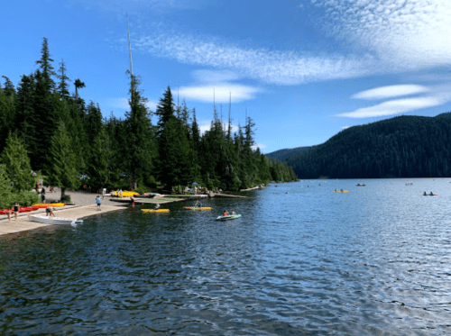 A serene lake surrounded by trees, with people kayaking and enjoying the water on a sunny day.