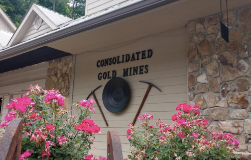 Sign for Consolidated Gold Mines with pickaxes and a pan, surrounded by pink flowers.