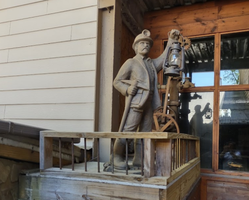 A statue of a miner holding a lantern, standing on a wooden platform near a building.