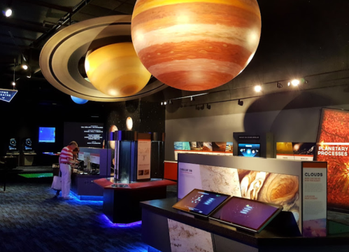 A space exhibit featuring models of planets, interactive displays, and educational panels in a dimly lit room.