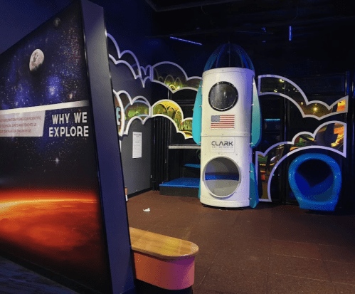 A colorful play area featuring a rocket-shaped structure and space-themed decor, with a sign about exploration.
