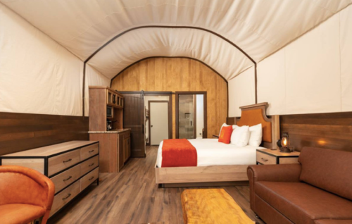 Cozy interior of a glamping tent featuring a bed, seating area, and wooden accents. Warm, inviting atmosphere.