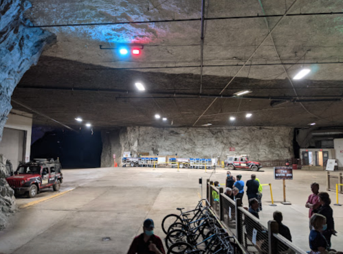 Interior of a large underground space with vehicles, lighting, and a line of bicycles in the foreground.