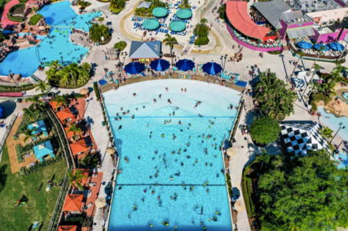 Aerial view of a vibrant water park with pools, sun loungers, and people enjoying the water on a sunny day.