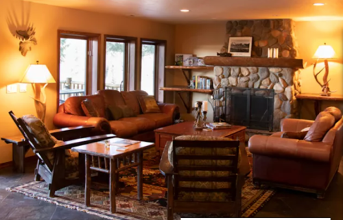 Cozy living room with a stone fireplace, leather sofas, wooden furniture, and warm lighting.