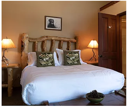 Cozy bedroom with a log bed, decorative pillows, and warm lighting from bedside lamps. A framed picture hangs on the wall.