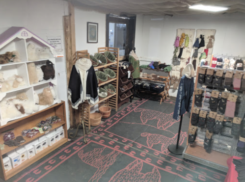 A cozy shop interior featuring shelves of clothing, accessories, and plush toys, with a patterned rug on the floor.