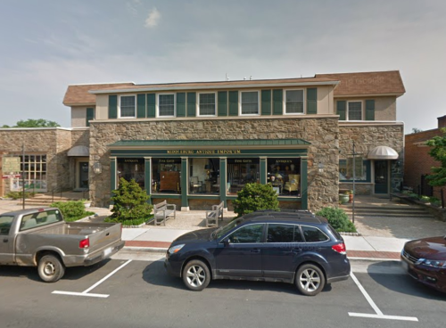 A stone building with large windows and a green awning, featuring shops on the ground floor and parked cars in front.