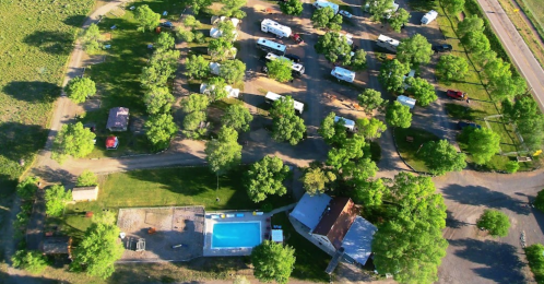 Aerial view of a campground with RVs, trees, a swimming pool, and a road nearby.