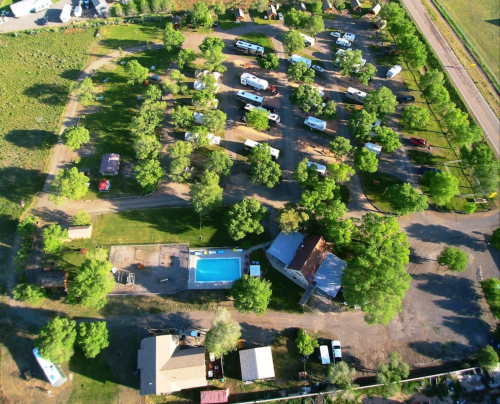 Aerial view of a campground with RVs, trees, a pool, and nearby roads.