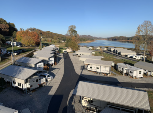 Aerial view of a campground with RVs and trailers near a lake, surrounded by trees and mountains in the background.