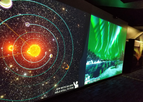 A digital display showing the solar system on one side and auroras over a lake on the other.