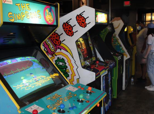 A row of vintage arcade machines, including "The Simpsons," in a lively gaming venue.