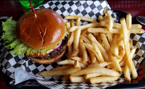 A juicy burger with lettuce, tomato, and onion, served with a side of golden French fries in a checkered basket.