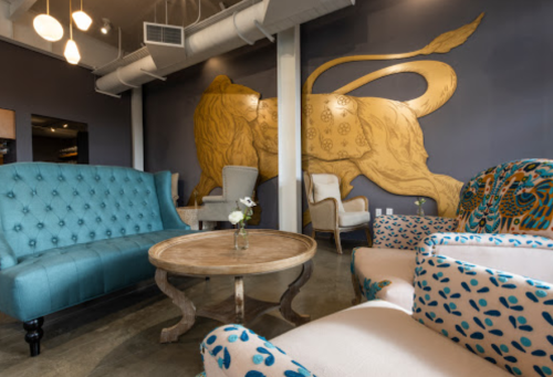 A stylish lounge with blue tufted sofas, a round table, and a large golden lion mural on the wall.