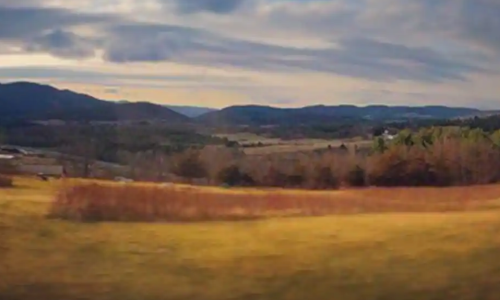 A scenic landscape featuring rolling hills, fields, and a cloudy sky during autumn.