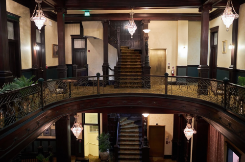 Elegant interior of a grand staircase with ornate chandeliers and wooden railings, showcasing a vintage architectural style.